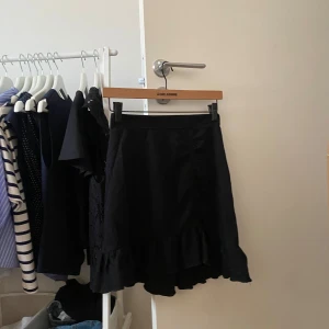 Svart volangkjol  - Supersnygg svart kjol från Gina Tricot med volangkant nertill. Kjolen är kort och har en lätt utsvängd form som ger en skön och trendig vibe. Perfekt att styla med en enkel topp eller stickad tröja.