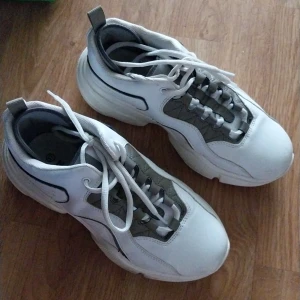 Chunky vita sneakers från NA-KD - Säljer ett par chunky sneakers från NA-KD i vitt och grått med bred sula och snörning. Skorna har en modern, sportig look med detaljer i syntetmaterial och textil. Perfekta för dig som gillar streetstyle och vill ha bekväma skor med attityd.