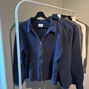 Mörkblå kofta från Ben Sherman - Säljer en mörkblå kofta från Ben Sherman i stickat material. Koftan har hel dragkedja framtill, klassisk krage och långa ärmar. Perfekt för lager-på-lager och enkel att matcha med olika outfits.