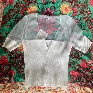 Vit ribbad kofta med meshdetaljer - Superfin vit kofta från ZARA med ribbad nederdel och transparent mesh upptill och på ärmarna. Knappar framtill och v-ringad hals. Kortärmad och figurnära passform, perfekt för en trendig look. Oanvänd och med prislapparna kvar. Storlek s 
