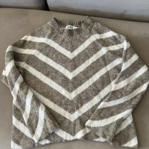 Beige och vit stickad tröja från ONLY - Säljer en stickad tröja från ONLY i beige och vitt med snygga breda, v-formade ränder. Tröjan har rund halsringning och långa ärmar. Perfekt för dig som gillar en chill och trendig look under höst och vinter.