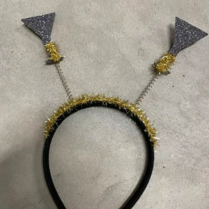 Glittrigt diadem med guld och silver - Diadem med svarta och glittriga silverpilar på spiralfjädrar. Omsluten av guldigt glitter som ger en festlig känsla. Perfekt accessoar för party eller nyårsfirande.