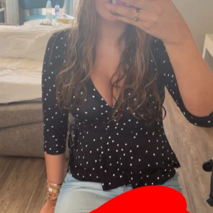 prickig söt blus - Snygg svart omlottopp med vita prickar och trekvartsärm. Toppen har v-ringning och knyt i sidan som ger en feminin siluett. Perfekt att styla med jeans eller kjol för en trendig look.