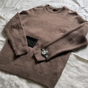 stickad tröja från Smog - Mysig beige stickad tröja från Smog i regular fit. Tröjan har rund halsringning, ribbade muddar och lång ärm. Perfekt för lager-på-lager och chill dagar. Enkel och stilren design som funkar till det mesta.