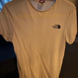 Vit t-shirt från The North Face XS - Vit t-shirt från The North Face i klassisk modell med rund hals och kort ärm. Diskret svart logga på bröstet. Skön och enkel stil, perfekt till jeans eller shorts. Tillverkad i mjuk bomull för en bekväm känsla hela dagen. 