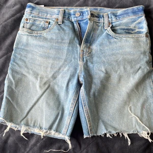 Levi's 502 ljusblå jeansshorts W34 - Ljusblå jeansshorts från Levi's modell 502 med klassisk femficksdesign och rå, fransig kant nedtill. Shortsen har normal passform och är tillverkade i slitstarkt denim. Perfekta för en avslappnad och cool look.