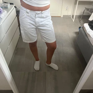 Vita cargo shorts med fickor - Vita cargo shorts med flera stora fickor på sidorna och bak, perfekta för dig som gillar praktiska detaljer. Shortsens raka passform och midwaist gör dem både bekväma och snygga. Tillverkade i bomull för en skön känsla under varma dagar.
