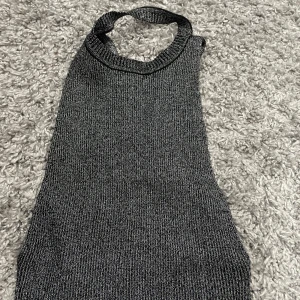 Glittrig stickad halterneck topp  - Snygg glittrig stickad halterneck topp från FB Sister i mörkgrått. Toppen har smala band som knyts i nacken och en croppad passform. Perfekt för dig som vill sticka ut med en trendig och cool look.