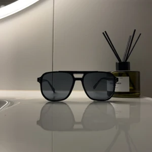 Svarta pilotbågar solglasögon - Snygga solglasögon med svarta pilotbågar och mörka glas. Klassisk aviator-stil med dubbla nitar vid bågens hörn och en cool brygga över näsan. Perfekta för att ge din look en edge i sommarvärmen.