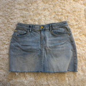 Ljusblå jeanskjol - Snygg ljusblå jeanskjol med klassiska fickor fram och bak, bälteshällor och rå, fransig kant nedtill. Kjolen har en enkel design med gylf och knapp framtill, perfekt för en avslappnad och trendig look. Storlek 158/164 men passar mig som vanligtvis har xs/s❤️