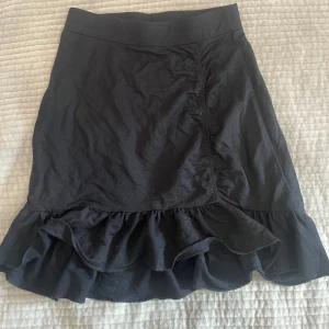 Svart volangkjol från Gina Tricot - Supersöt svart kjol från Gina Tricot med volangkant nertill. Kjolen är kort och har en enkel, stilren design. 📩 Skicka gärna ett meddelande vid frågor eller om du vill ha flera bilder! 🌸😊 📦 Jag skickar snabbt och packar alltid med omsorg!