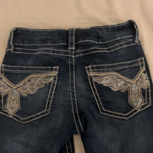 Gina tricot mörkblå jeans med broderade fickor - Snygga mörkblå jeans med kontrastsömmar och unika broderade bakfickor med paljettdetaljer. Jeansen har klassisk femficksdesign och normal passform. Perfekta för dig som vill sticka ut med coola detaljer. Priset kan diskuteras 