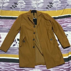 Brun rock från Minimum, storlek S - Snygg brun rock från Minimum i storlek S. Jackan har klassisk krage, knäppning med svarta knappar och två fickor med lock framtill. Materialet är mjukt och känns som bomull, perfekt för dig som gillar stilrena och enkla plagg med lite edge.