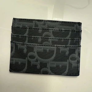 Svart plånbok med mönster - Slimmad svart plånbok med flera kortfack och ett coolt grafiskt mönster i grått. Tillverkad i syntetmaterial med stilren design som passar perfekt i fickan. Passar tjejer och killar!