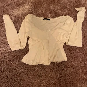 Söt cremefärgad/ vit blus från Gina Tricot - Supersöt cremefärgad/ vit blus från Gina Tricot med lång ärm, spetsdetaljer längs halsringningen och en liten rosett framtill. Blusen har en lätt utsvängd nederdel och romantisk vibe, perfekt att styla med jeans eller kjol.