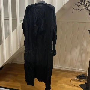 Svart långklänning från Saint Tropez - Säljer en svart långklänning från Saint Tropez med långärmade och skrynklig look. Klänningen har en flowy passform och är tillverkad i ett lätt material som ger en cool vibe. Perfekt för dig som gillar en enkel men edgy stil. Frakt ej inklusive.