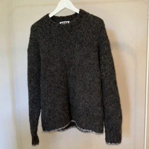 Mörkgrå stickad tröja från HOPE - Säljer en mörkgrå stickad tröja från HOPE med grov, fluffig struktur. Tröjan har rund hals och långa ärmar, samt råa kanter vid ärmslut och nederkant för en cool, avslappnad vibe. Köpt för 4000