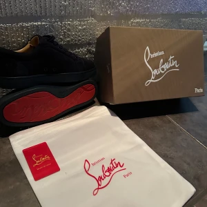 Mörkblå Christian Louboutin sneakers - Snygga mörkblå sneakers från Christian Louboutin i mjuk mocka med klassisk röd signatursula. Skorna har rund tå, platt sula och snörning. Insidan är beige och har guldfärgad logga. Perfekt för dig som vill sticka ut med exklusiv stil. Ny pris 6.800kr 