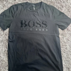 Svart Hugo Boss t-shirt med logga - Svart t-shirt från Hugo Boss med stor  BOSS-logga på bröstet och rund hals. Klassisk passform och korta ärmar, tillverkad i mjuk bomull som känns skön mot huden.
