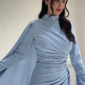 Ljusblå långklänning med pärlor - Säljer en elegant ljusblå långklänning med högt halslinje dekorerad med pärlor. Klänningen har långa ärmar och vackra draperingar över hela kroppen som ger en lyxig känsla. Perfekt för dig som vill sticka ut med stil på speciella tillfällen.