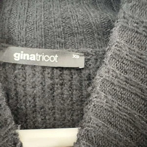 Svart stickad offshoulder tröja Gina Tricot - Cool svart stickad tröja från Gina Tricot i storlek XS. Tröjan har offshoulder-design med höghalsad krage och långa ärmar. Ribbstickad struktur och croppad passform ger en trendig vibe. Perfekt för dig som gillar att sticka ut med din stil.