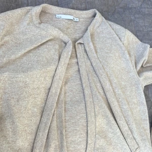 Beige kofta i mjuk bomull - Säljer en stilren beige kofta från lager 157 i storlek S. Koftan är öppen framtill utan knappar med mjuka band man kan knyta och har långärmade ärmar. Materialet är mjuk bomull som känns skönt mot huden. Perfekt för lager-på-lager och chill dagar.