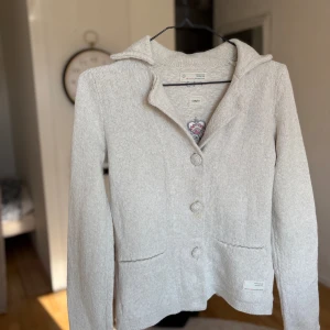 Beige cardigan jacka Odd Molly - Snygg beige cardigan jacka från Odd Molly med broderad logga på ryggen och insidan. Jackan har krage, tre knappar framtill och två fickor. Stickad i mjukt material, perfekt för lager på lager. 