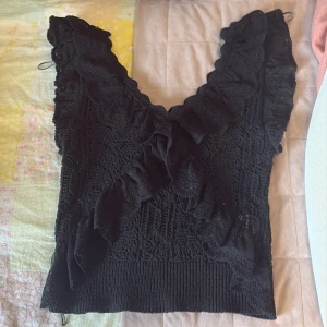 Svart spetsblus med volanger från Zara - Svart blus från Zara i medium med snygga spetsdetaljer och volanger framtill. Blusen har v-ringad hals och är ärmlös, vilket ger en cool och feminin vibe. Materialet är spets och ribbad nederkant för extra stilpoäng. Perfekt för dig som gillar statement-plagg. För mer frågor är det bara att dma💕