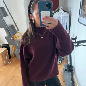 Vinröd stickad tröja från Zara - Säljer en vinröd stickad tröja från Zara i storlek L. Tröjan har en hög, ribbad hals och långa ärmar med loose passform. Materialet är mjukt och värmande, perfekt för kyliga dagar. Enkel och stilren design utan mönster eller detaljer.