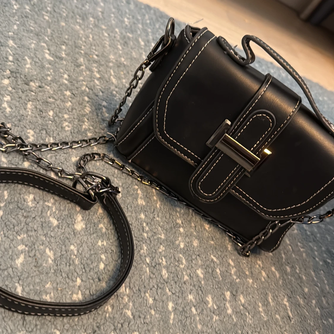 Svart axelväska med kedja och vita sömmar