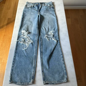 Loose fit jeans, Denim, ljusblå - Ljusblå jeans med loose straight passform och hög midja. Snygga slitningar och hål på båda benen framtill samt slitna benslut. 