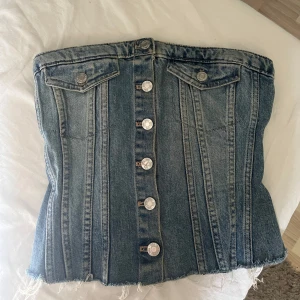 Jeanskorsett från Zara med knappar - Säljer en snygg jeanskorsett från Zara i klassisk blå denim i storlek XS. Toppen har silverfärgade knappar framtill. Säljer pågrund av att den har blivit för liten för mig 