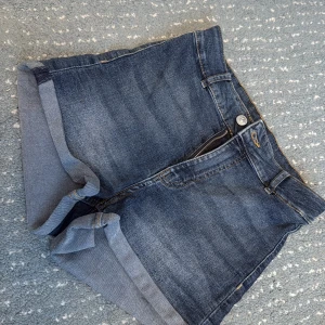 Mörkblå jeansshorts från Divided - Snygga mörkblå jeansshorts från Divided by H&M i klassisk femficksmodell. Shortsen har uppvikta benslut, bälteshällor och dragkedja med knapp framtill. Perfekta för sommardagar och enkla att matcha med allt.