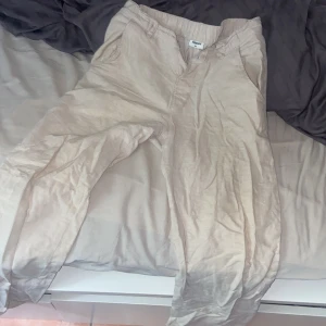 Beige linnebyxor från Kappahl - Snygga beige linnebyxor från Kappahl i storlek 164. De har elastisk midja, knappstängning och fickor både fram och bak. Perfekta för chill dagar och har en avslappnad passform med rak siluett. Materialet är linne som ger en skön och luftig känsla.