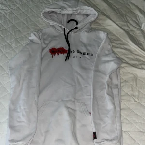 Vit hoodie Supply & Demand NYC - Vit hoodie från Supply & Demand med tryck i svart och rött på bröstet där det står 'Supply and Demand New York City'. Hoodien har svart snörning i huvan, stor magficka och ribbade muddar. Perfekt för chill dagar och streetwear-stil.