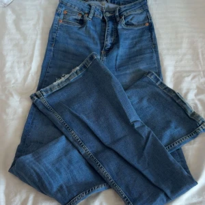 Levi's 501 blå jeans - Klassiska Levi's 501 jeans i blå denim med raka ben och fem fickor. Byxorna har knappgylf och orangea nitar vid fickorna. Perfekta för dig som gillar tidlös stil och vill ha ett par jeans som funkar till allt. Snyggt slitna detaljer vid benslut.