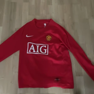 Manchester United Ronaldo 7 långärmad tröja - Säljer en klassisk Manchester United fotbollströja med Ronaldo 7 på ryggen. Tröjan är röd med vita detaljer, långärmad och har AIG som sponsor på framsidan. Officiellt klubbmärke på bröstet och Nike-logga. Perfekt för fans av Ronaldo och United.