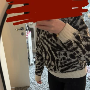 Stickad tröja med zebramönster - Säljer en stickad tröja med coolt zebramönster i svart och beige. Tröjan har långärmad design och ribbade muddar vid ärmslut och nederkant. Perfekt för dig som vill sticka ut med ett djuriskt mönster och samtidigt hålla dig varm.