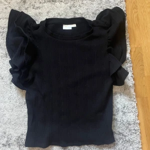 Svart ribbad topp med volangärmar - Snygg svart topp från Gina Tricot med ribbad struktur och volangärmar. 