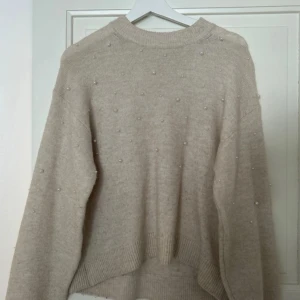 Beige stickad tröja med pärlor H&M - Säljer en beige stickad tröja från H&M i storlek XS. Tröjan har rund hals, långa ärmar och är dekorerad med små pärlor över hela framsidan. Mjuk och skön passform med ribbade muddar vid hals, ärmslut och nederkant. 