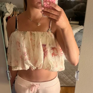 Blommig volangig linnetopp i pastell från h&m - Supersöt och luftig linnetopp med volangig ballongform och tunna axelband. Toppens tyg är vitt med blommigt mönster i pastelliga rosa, lila och gröna toner. Perfekt för varma dagar och ger en romantisk vibe till din outfit.