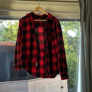 Röd och svart rutig skjorta 157 M - Snygg röd och svart rutig skjorta från 157 i storlek M. Skjortan har klassisk krage, långa ärmar och knappar framtill. Perfekt för dig som gillar en avslappnad stil med lite edge. Materialet känns mjukt och bekvämt mot huden.