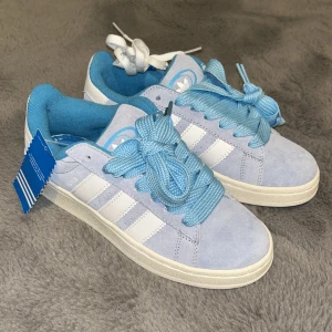 Adidas Campus ljusblå sneakers 37 1/3 - Adidas Campus sneakers i ljusblå mocka med vita klassiska stripes och tjocka blå skosnören. Insidan är fodrad i blått tyg och skon har en platt vit sula. Ikonisk Adidas-logga på plösen och extra vita skosnören medföljer. Perfekt för dig som gillar retrostil och färg.