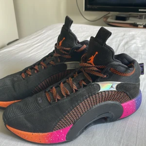Svarta Air jordan 35 - Säljer ett par svarta Air Jordan basket sneakers med orange detaljer och snörning. Skorna har en cool gradient sula i lila, rosa och orange med vita prickar, samt holografiska inslag vid sidan. Materialet är en mix av syntet och mocka, med rund tå och platt sula. Perfekt för dig som gillar att sticka ut. Det står strorlek 44 i men passar även 43. Original pris 1899, men har haft dom hemma i ett flertal år nu.