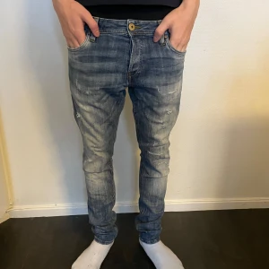 Blå jeans med slitningar - Snygga blå jeans med en cool slitningseffekt. De har en klassisk femficksdesign och en knappgylf. Perfekta för en avslappnad stil.