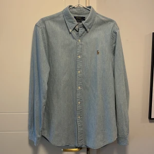 Ljusblå skjorta från Ralph Lauren - Säljer en stilren ljusblå skjorta från Ralph Lauren i slim fit. Skjortan har långa ärmar och en klassisk krage med knappar. Perfekt för en elegant och avslappnad look.