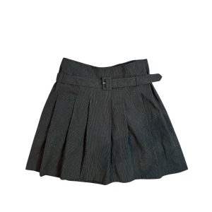 Lowwaist knäkjol med skärp - Snygg svart knäkjol med skärp i kostymliknande material. Den har diskutera ränder som jag hoppas att man ser tydligt på bild. Även en kedja i sidan för att underlätta när man ska ta på och av. Köpt second hand men tyvärr lite för stor till mig och därav aldrig använd. Storlek: 36