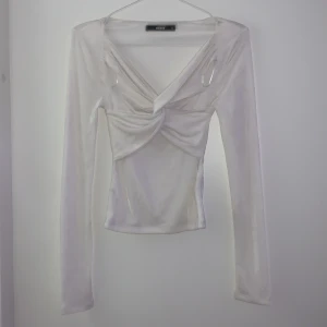 Vit långärmad topp från BikBok - Säljer en elegant vit långärmad topp från BikBok i storlek XS. Toppen har en v-ringad design med knytning framtill som ger en snygg detalj. Perfekt för att lyfta din outfit med en touch av stil.