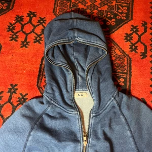 Blå Acne fullzip - Säljer en snygg blå hoodie från Acne med dragkedja och fickor framtill. Perfekt för en avslappnad stil. Huvan ger extra komfort och värme.