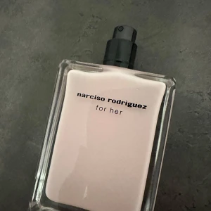 Narciso Rodriguez For Her Parfym - Elegant parfymflaska från Narciso Rodriguez med en stilren design. Flaskan är rektangulär med en ljusrosa nyans och svart text. Perfekt för den som söker en sofistikerad doftupplevelse. 50 ml endast testas eu de perfume